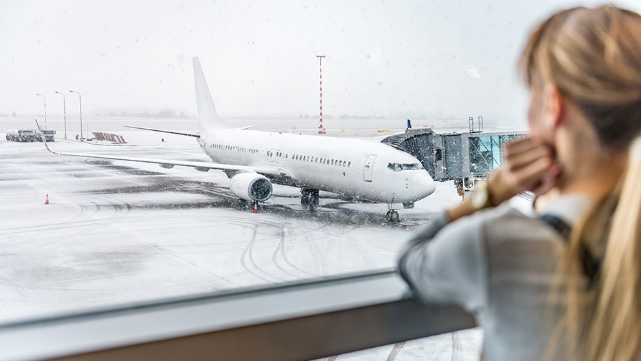 woman looks out airport window at airplane in snow