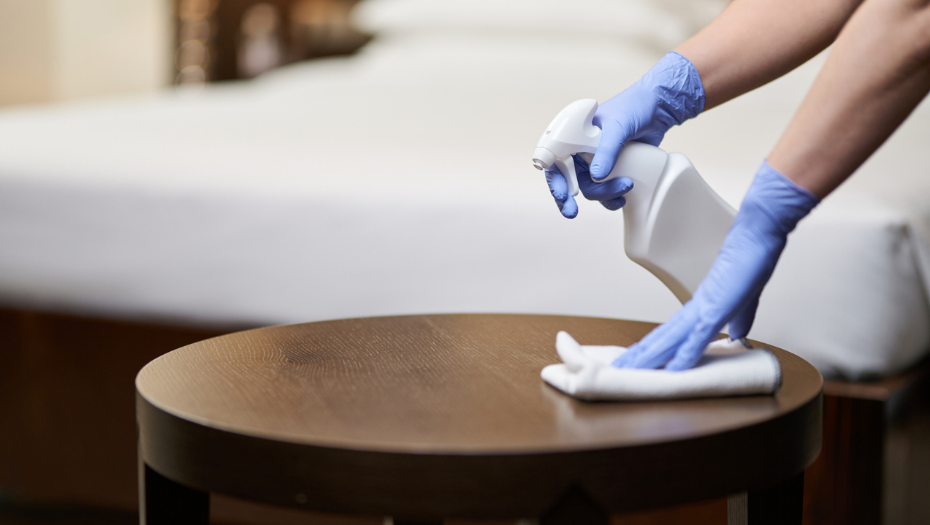 gloved hands cleaning table of hotel room per COVID protols